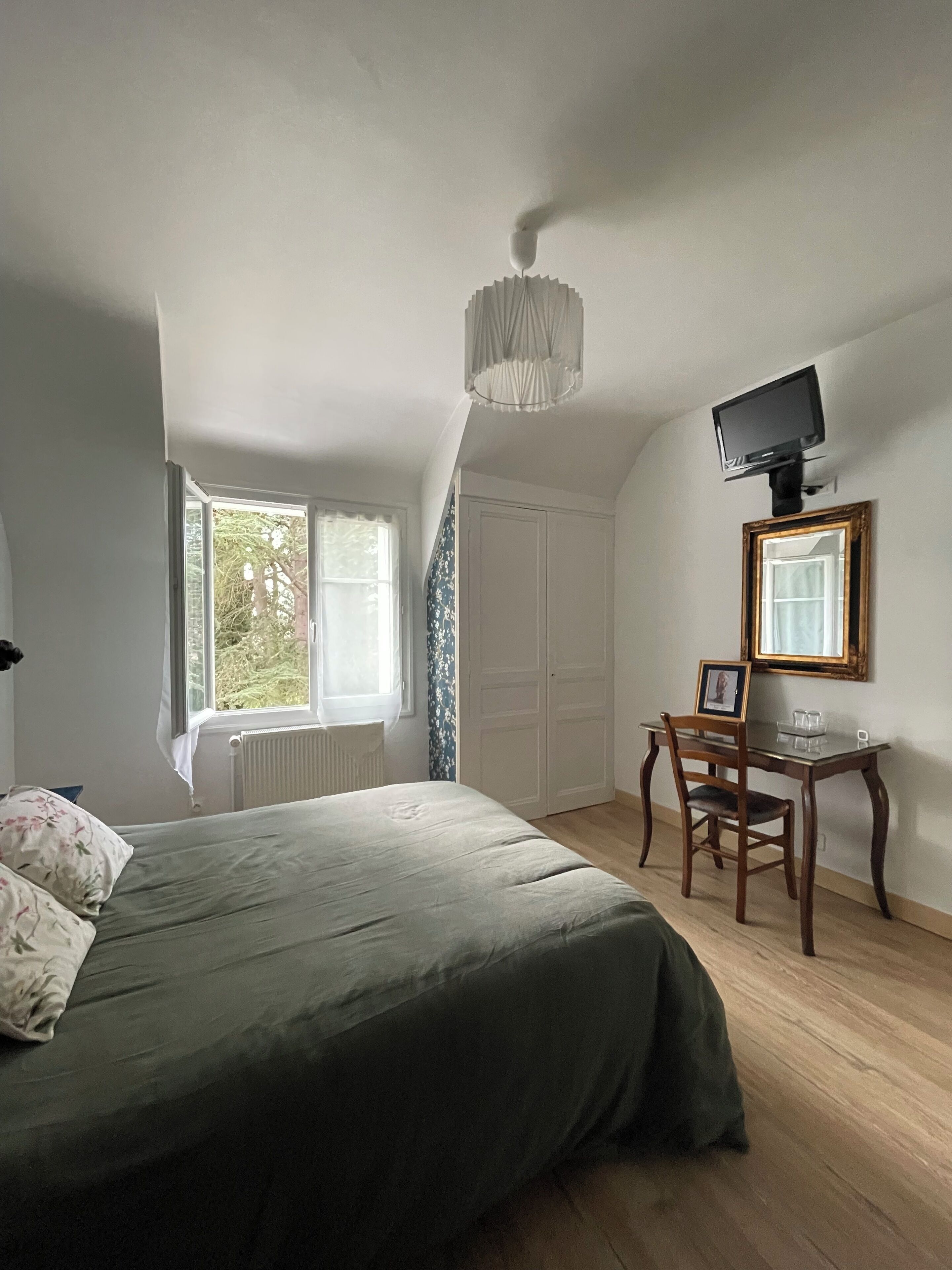 Un dormitorio con cama, escritorio, silla, televisor y ventana.