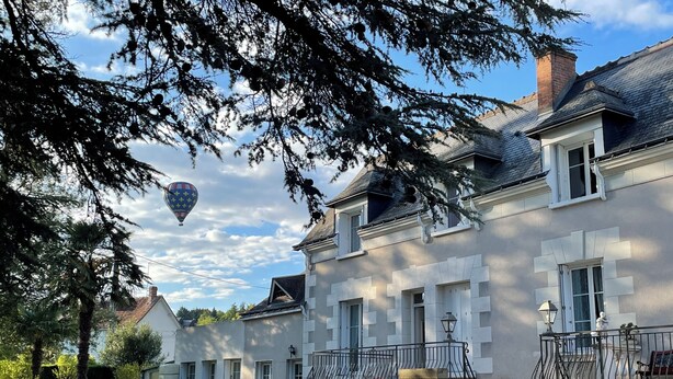Ein großes, zweistöckiges Haus mit Balkon und einem Heißluftballon am Himmel.