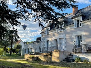 A large, two-story house with a balcony and a hot air balloon in the sky. - Aux Chambres des Dames (Chisseaux)