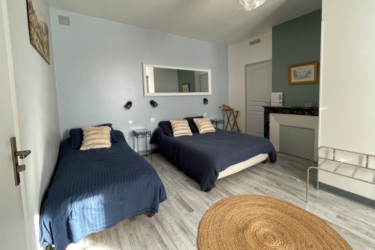 Une chambre avec deux lits, un tapis rond en fibres naturelles, un miroir et un coin cuisine.