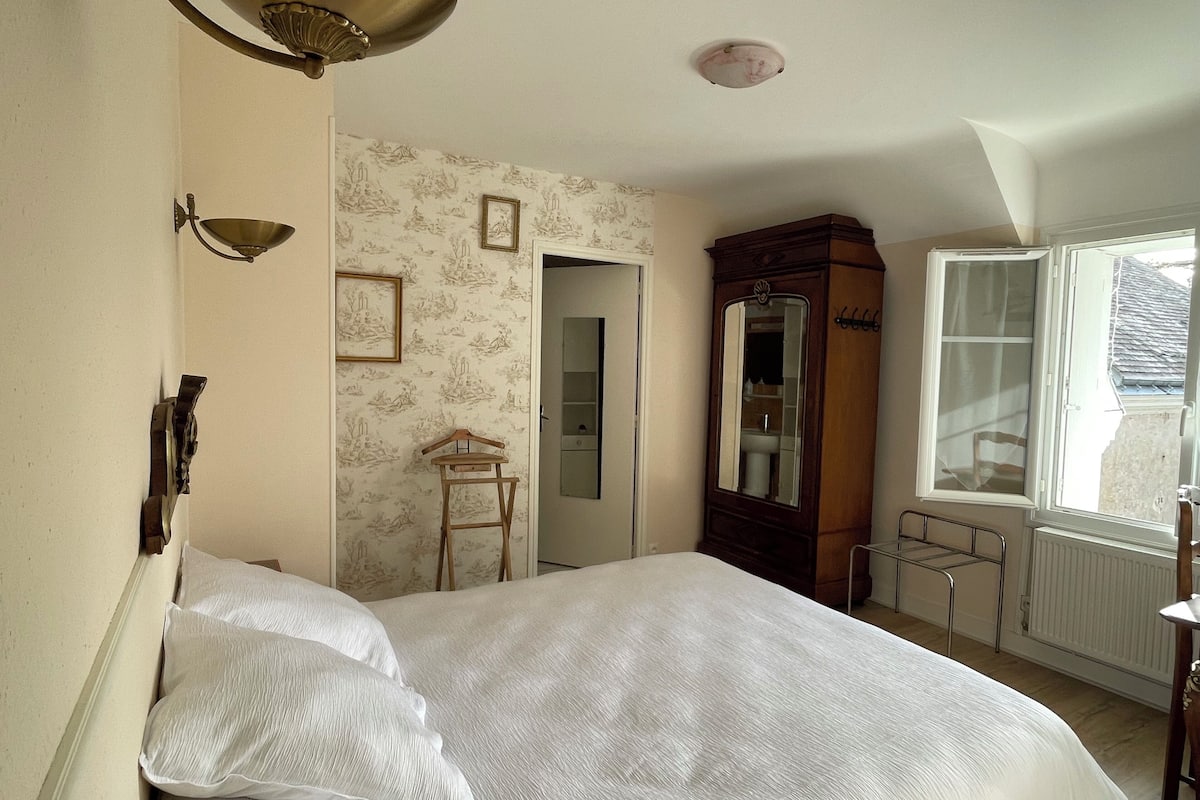 Une chambre à coucher comprenant un lit, une armoire, un miroir, un radiateur et une fenêtre.