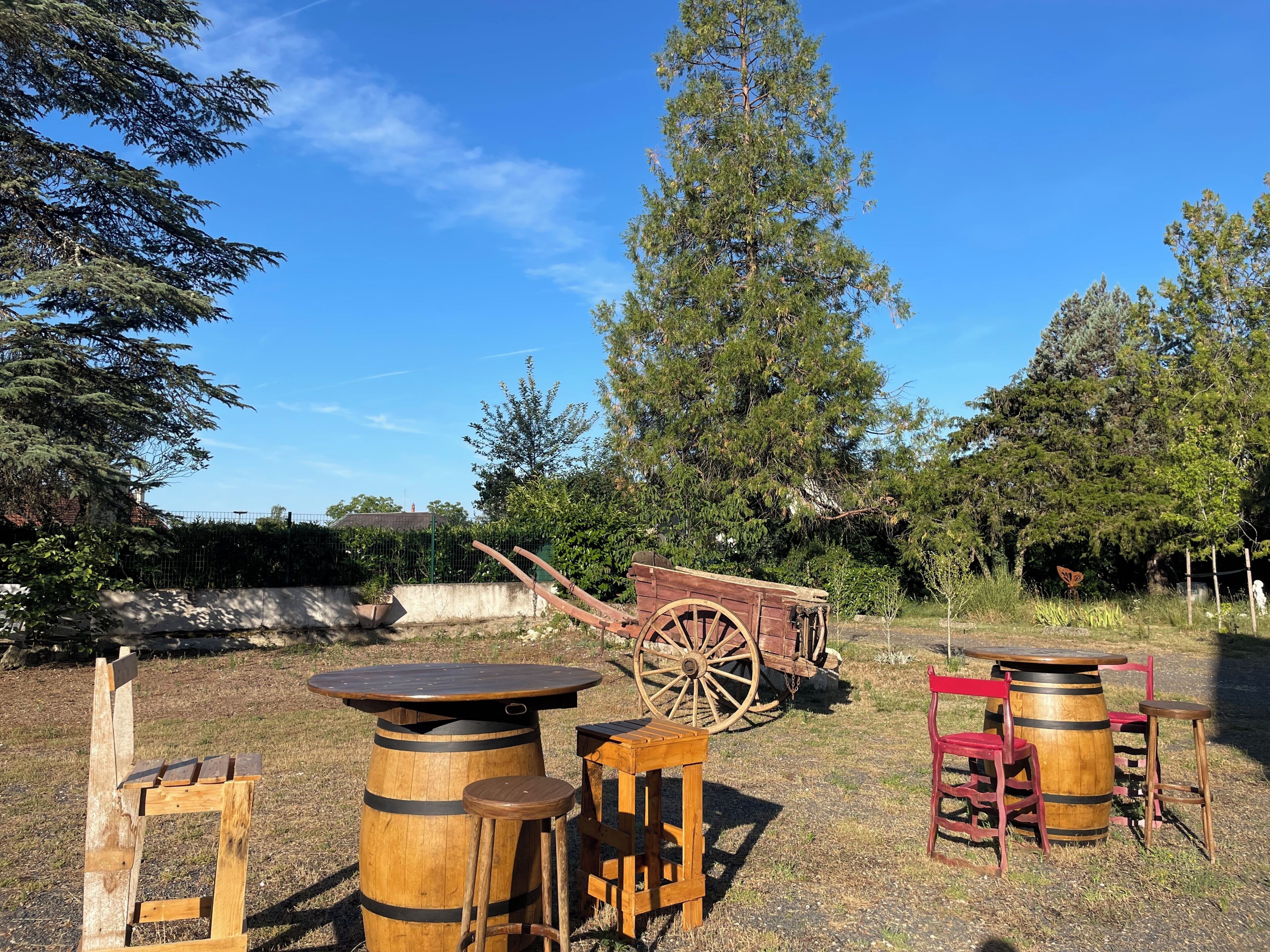 Outdoor wooden furniture including a table and chairs, a barrel, and a wagon wheel.