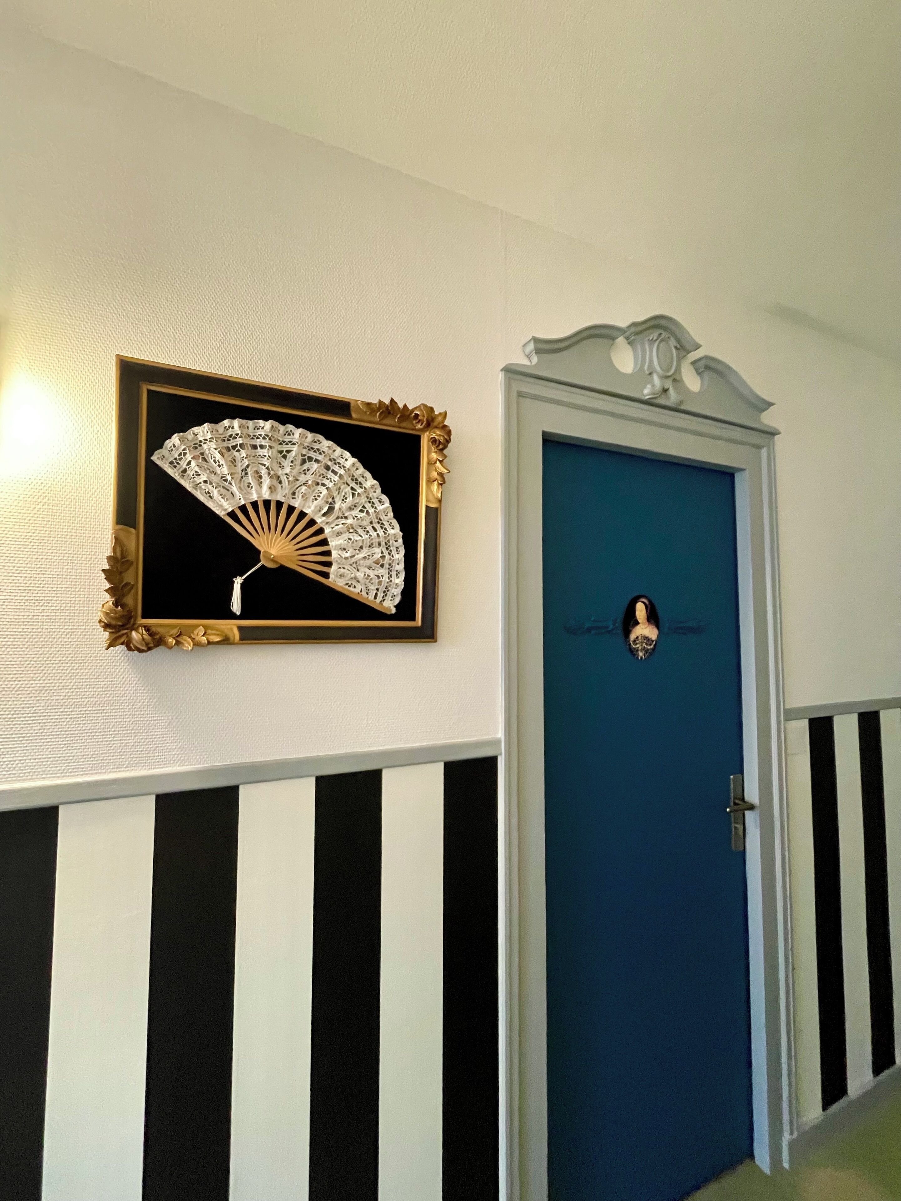 A hallway with a blue door, a framed fan, and black and white striped walls.