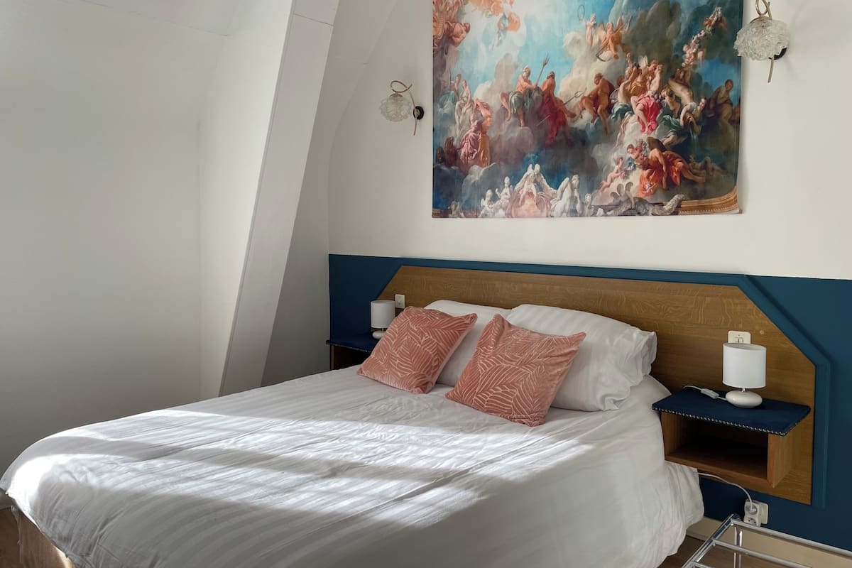 Une chambre à coucher avec un grand lit, deux tables de chevet, une lampe fixée au mur et une fresque peinte au plafond.