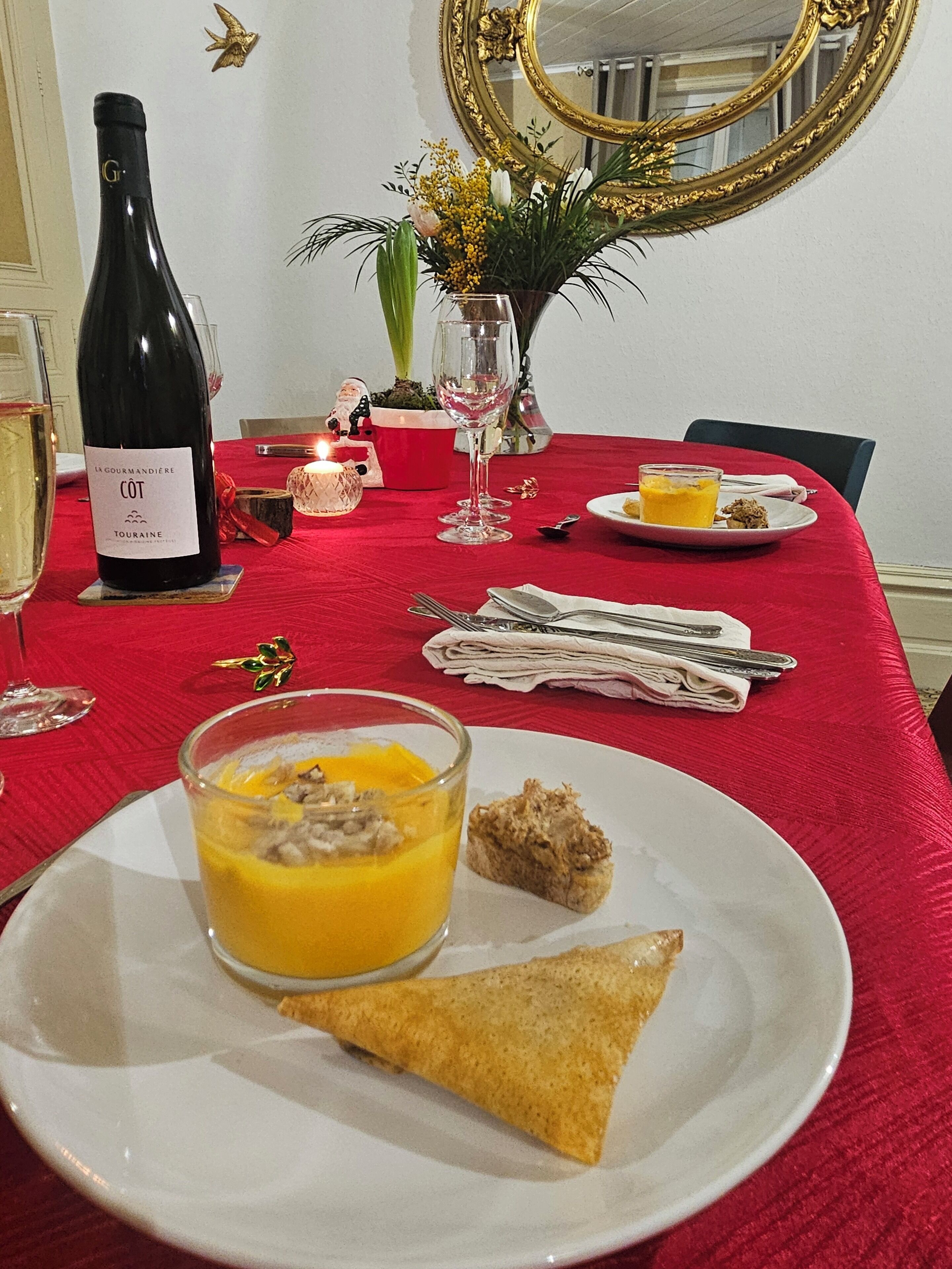 Et spisebord dækket med en vinflaske, et glas appelsinjuice, en tallerken med en sandwich og et wienerbrød, samt et lys.