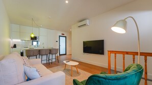 Un salon moderne avec un canapé, un fauteuil vert, une table basse et un téléviseur fixé au mur.