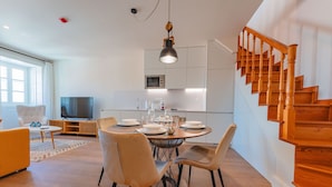 A modern living room with a dining area, wooden staircase, and a kitchen with a microwave. - FLH Funchal A Quinta do Conde Flat II (Funchal)