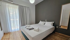 Een moderne slaapkamer met een groot bed, houten vloeren en uitzicht op het buitenleven door dunne gordijnen.