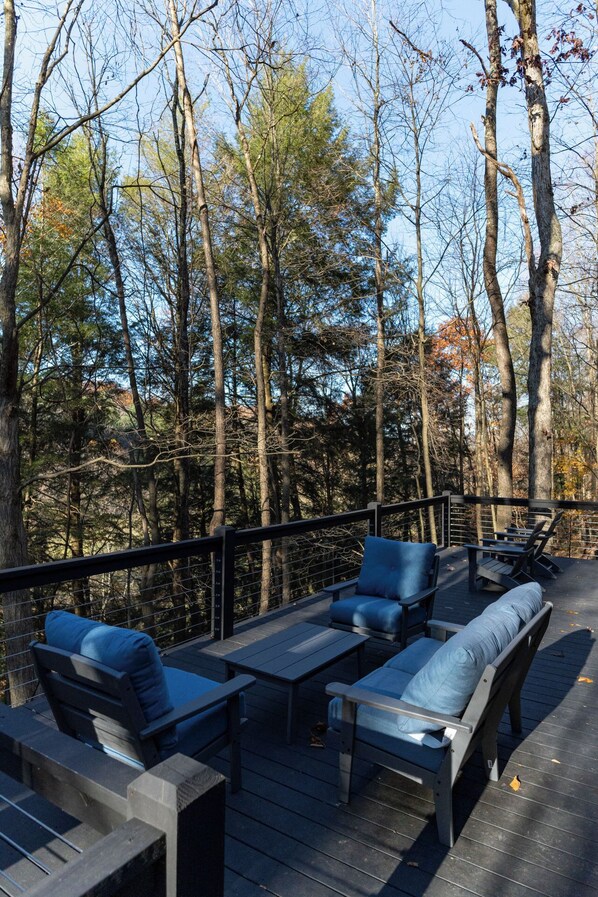 An outdoor deck with seating and a railing, surrounded by trees. - Fauna Bluff, A cliffside 2-bedroom modern cottage overlooking a bubbling stream. (Loudonville)
