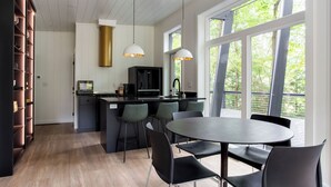 A modern kitchen with a central island, bar stools, and a dining table with chairs. - Fauna Bluff, A cliffside 2-bedroom modern cottage overlooking a bubbling stream. (Loudonville)