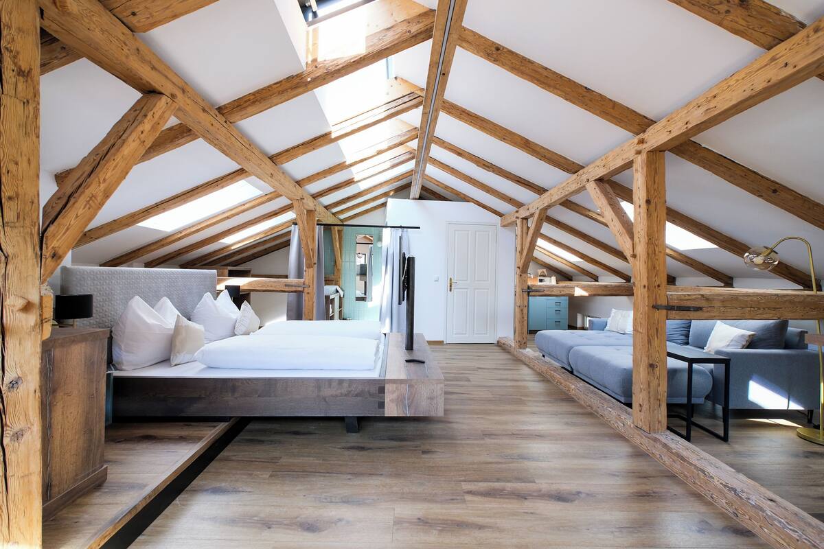 Une chambre à coucher de style loft avec des poutres apparentes, un lit, un canapé et un bureau.