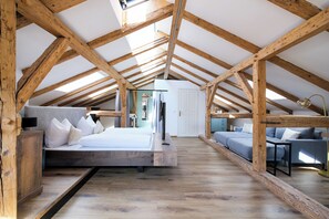 A loft bedroom with exposed wooden beams, a bed, a sofa, and a desk.