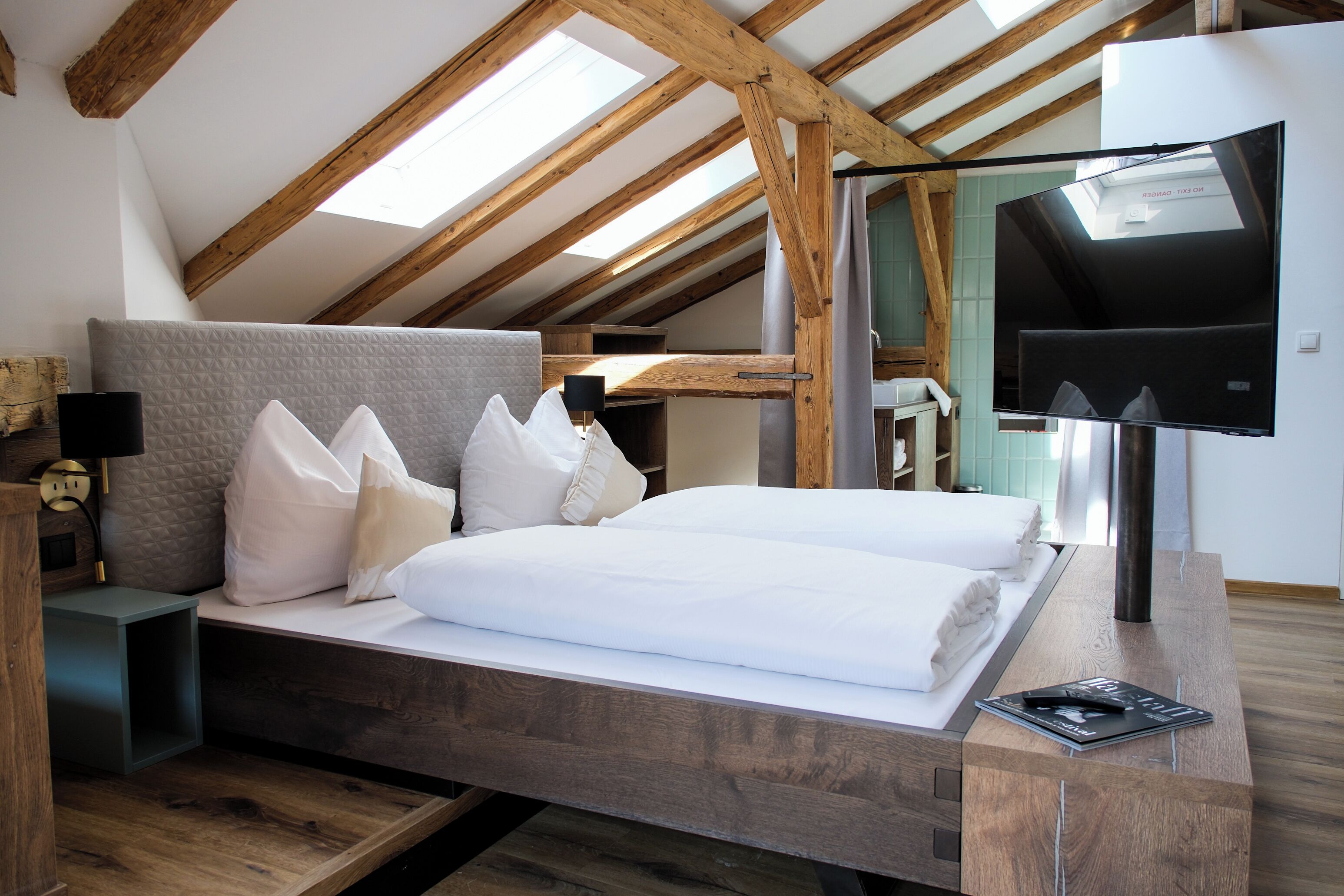 A bedroom with a wooden ceiling, a bed with white bedding, a bedside table with a lamp, and a TV on a stand.