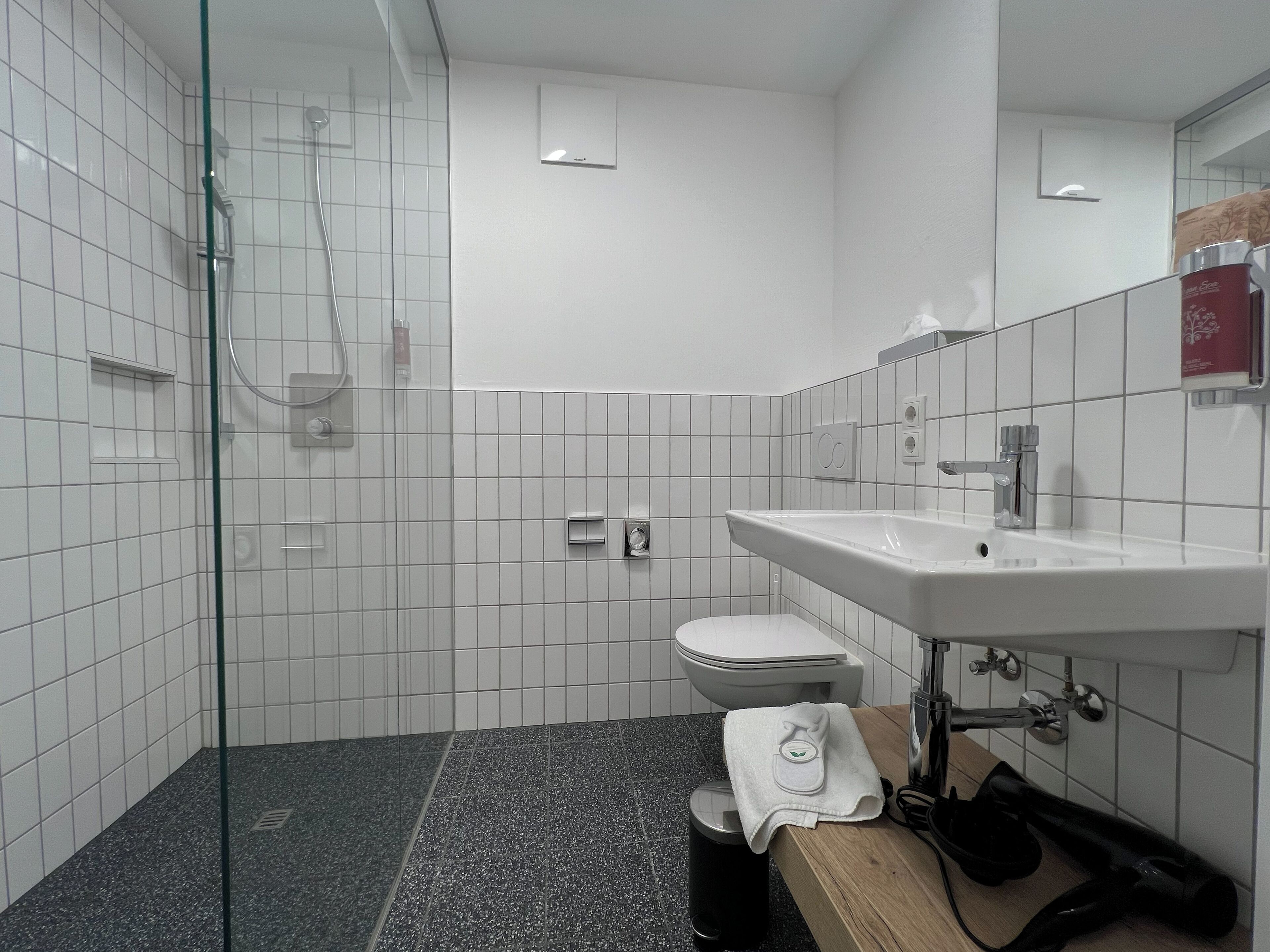 Un baño moderno con ducha envuelta en vidrio, inodoro blanco y lavamanos con espejo.