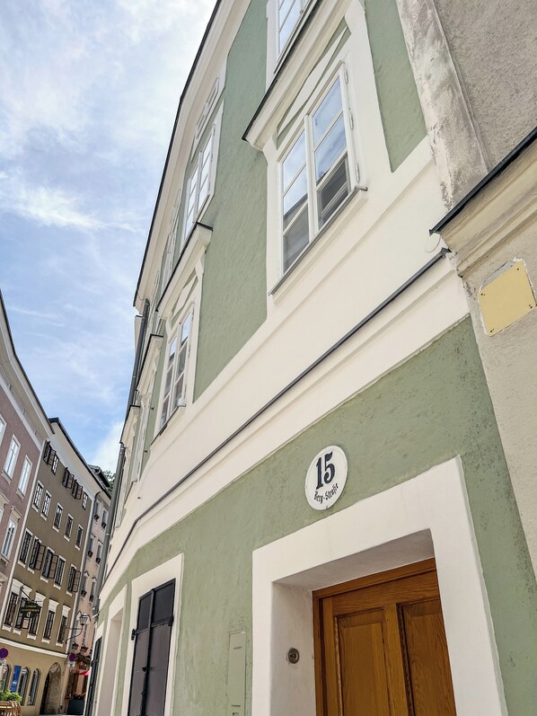 A building with a green facade, a visible door, and a window with a number plaque.
