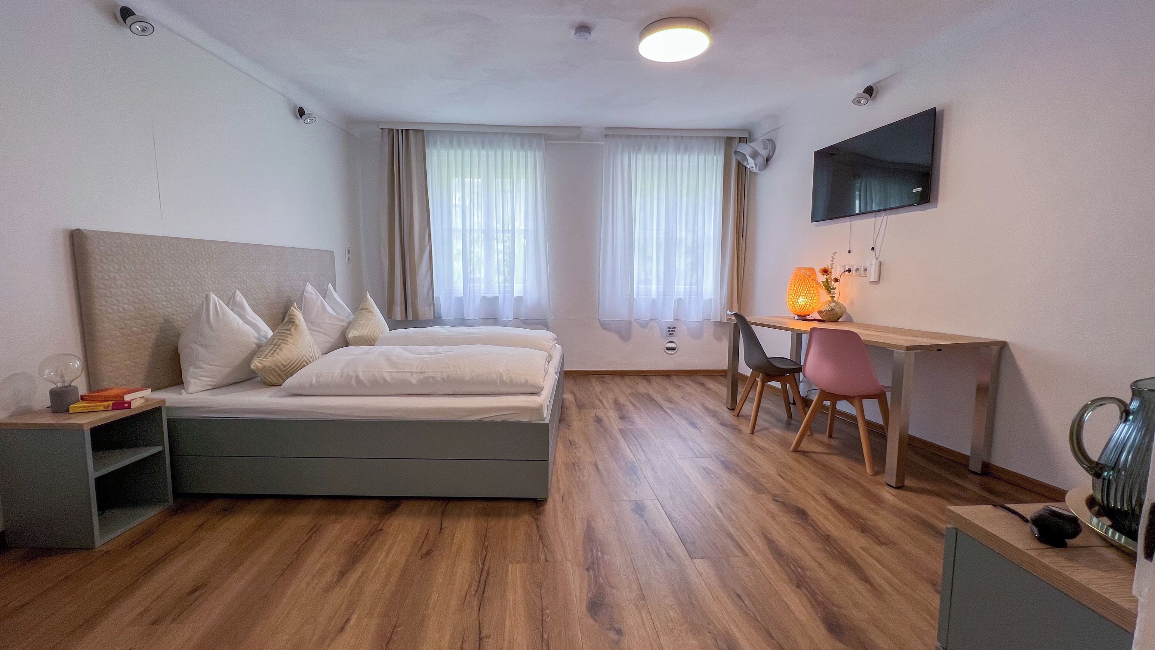 A bedroom with a bed, a desk, a chair, and a TV on the wall.