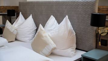 A neatly made bed with white linens and pillows, a grey headboard, and a bedside table with a lamp.