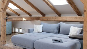 A loft bedroom with a wooden ceiling and skylights, a gray sofa bed, and a wooden floor. - Apartment Salzburg - Bergstrasse (Salzburg)