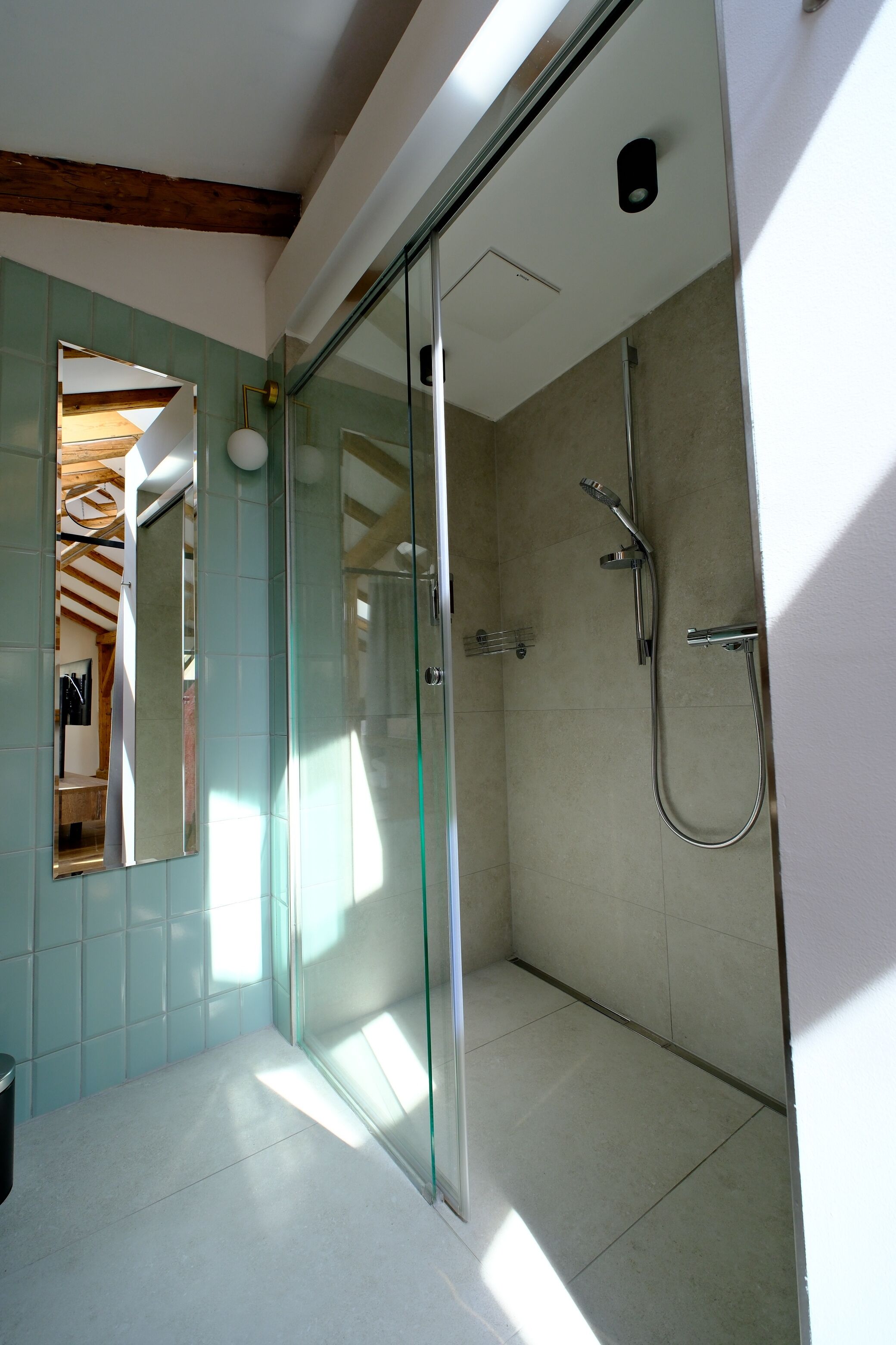 Un baño moderno con cabina de ducha de vidrio, una lámpara de techo visible y suelo de baldosas.