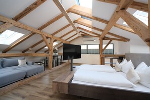 A loft bedroom with a wooden ceiling, a bed, a sofa, and a TV.