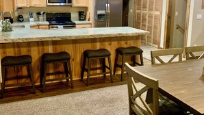 Una cocina moderna con armarios de madera, una isla grande con taburetes de bar, electrodomésticos de acero inoxidable y un comedor con mesa y sillas de madera.