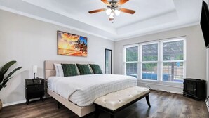 Ein Schlafzimmer mit einem Bett, einer Bank, einem Nachttisch, einem Deckenventilator, einem Gemälde und einem Fenster mit Jalousien.