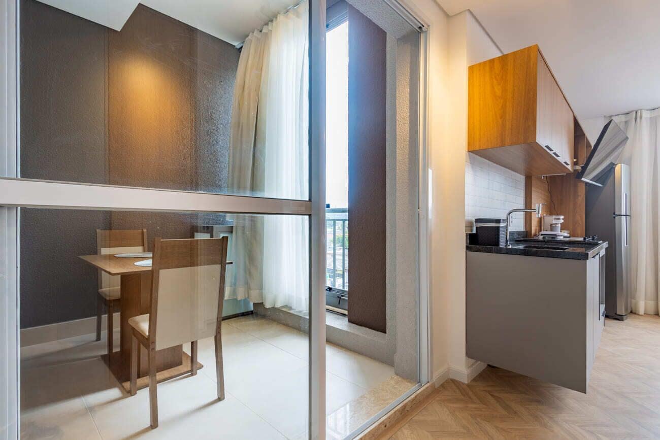 Una cocina moderna con horno empotrado, un comedor con mesa y sillas, y un puertas corredera de vidrio que da a un balcón.