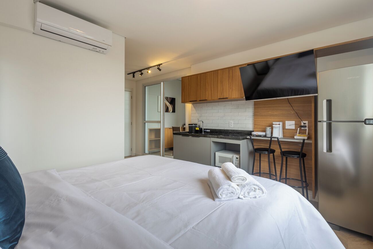 Ein modernes Hotelzimmer mit einem großen Bett, einer Küchenzeile mit Kühlschrank und einer Essecke mit Barhocker.
