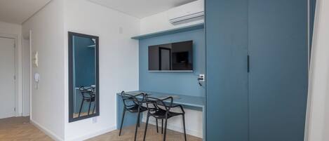 Quarto com piso de madeira em padrão herringbone, uma escrivaninha com duas cadeiras, um espelho grande e uma parede azul.