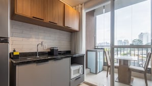 Une cuisine moderne avec un plan de travail noir, des armoires grises et un four à micro-ondes. Une fenêtre offre une vue sur les bâtiments à l’extérieur.