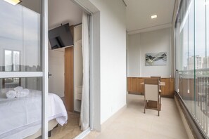 A modern hotel room with a bed, a desk, and a chair. There is a large window with a view of buildings.