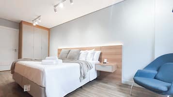 A modern hotel room with a large bed, bedside tables, a chair, and a wardrobe.