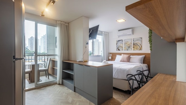 Une chambre d’hôtel de taille réduite, comprenant un lit, un petit bureau, une chaise et un balcon avec une table et des chaises.
