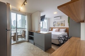 Une chambre d’hôtel de taille réduite, comprenant un lit, un petit bureau, une chaise et un balcon avec une table et des chaises.