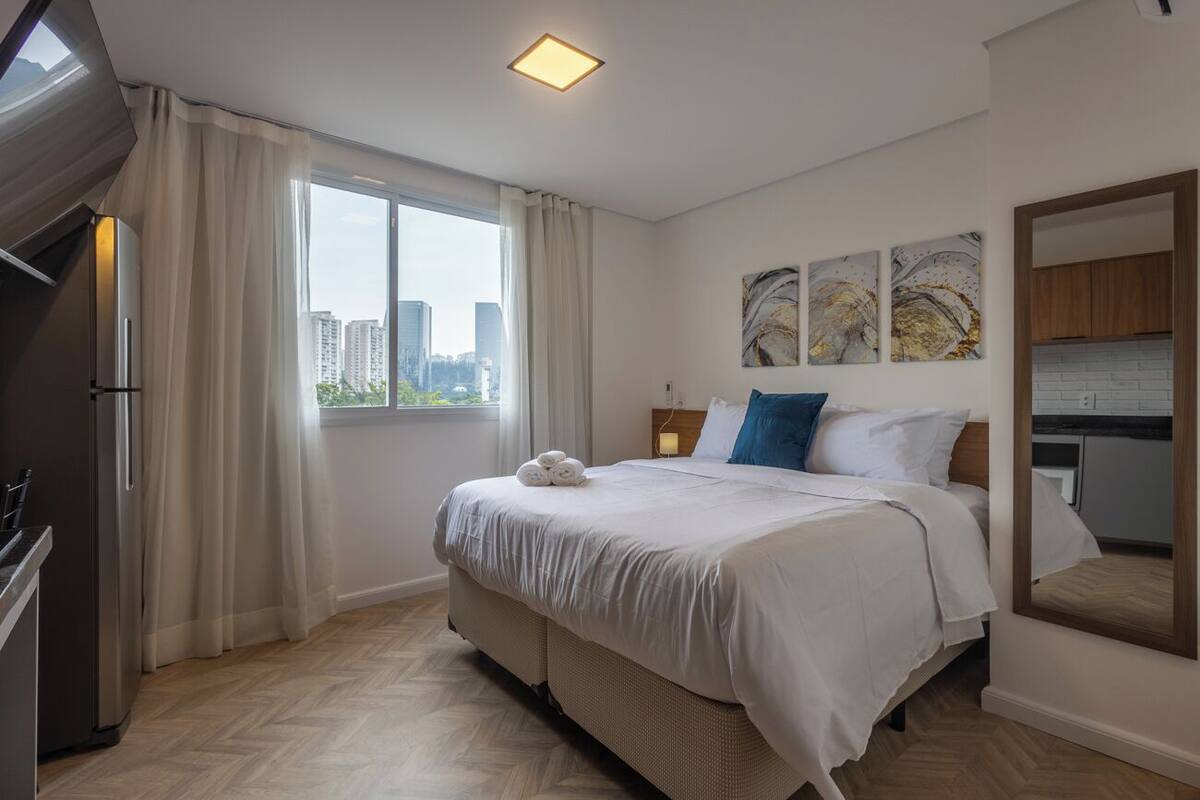 Une chambre d’hôtel moderne dotée d’un grand lit, offrant une vue sur la ville, et comprenant un réfrigérateur ainsi que des œuvres d’art accrochées au mur.