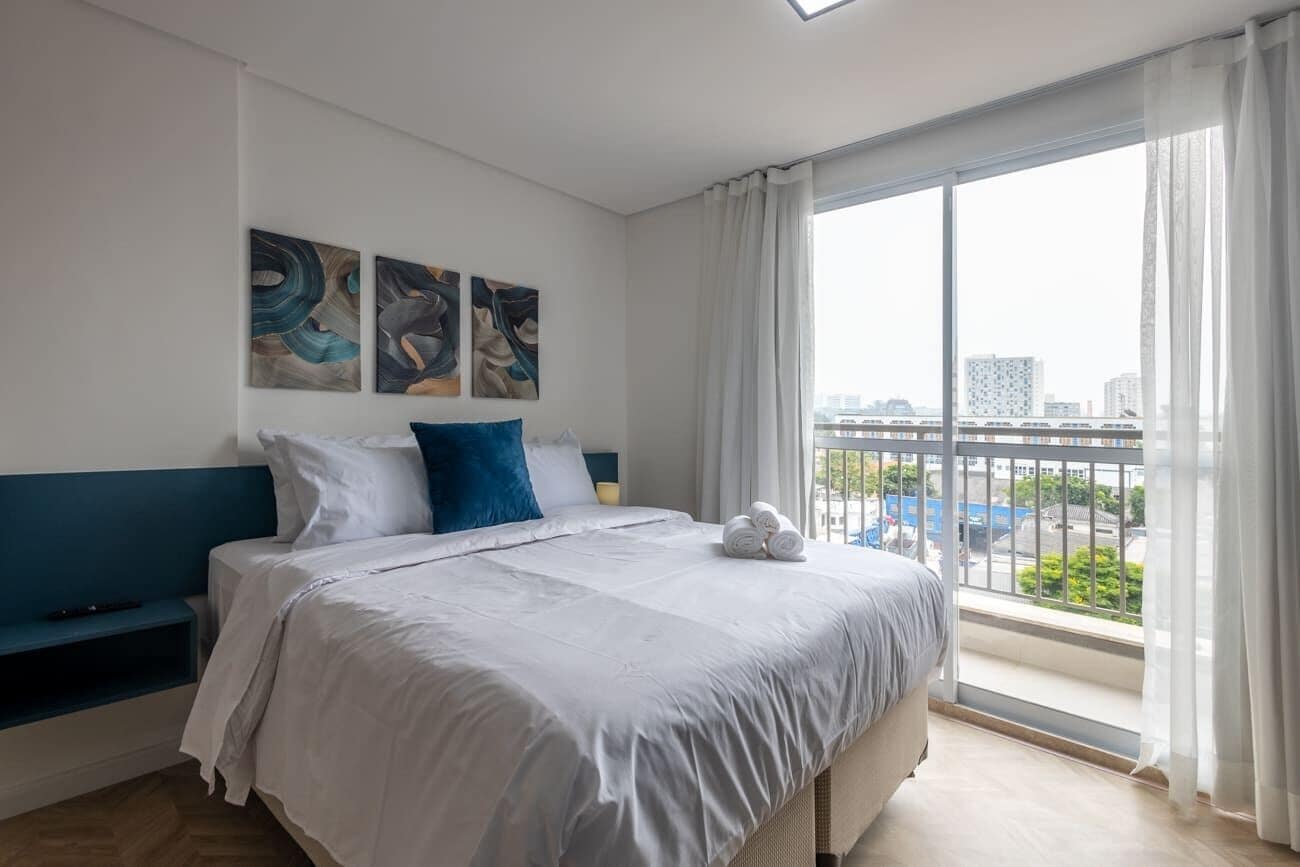 A modern hotel room with a large bed, a view of the city, and abstract art on the wall.