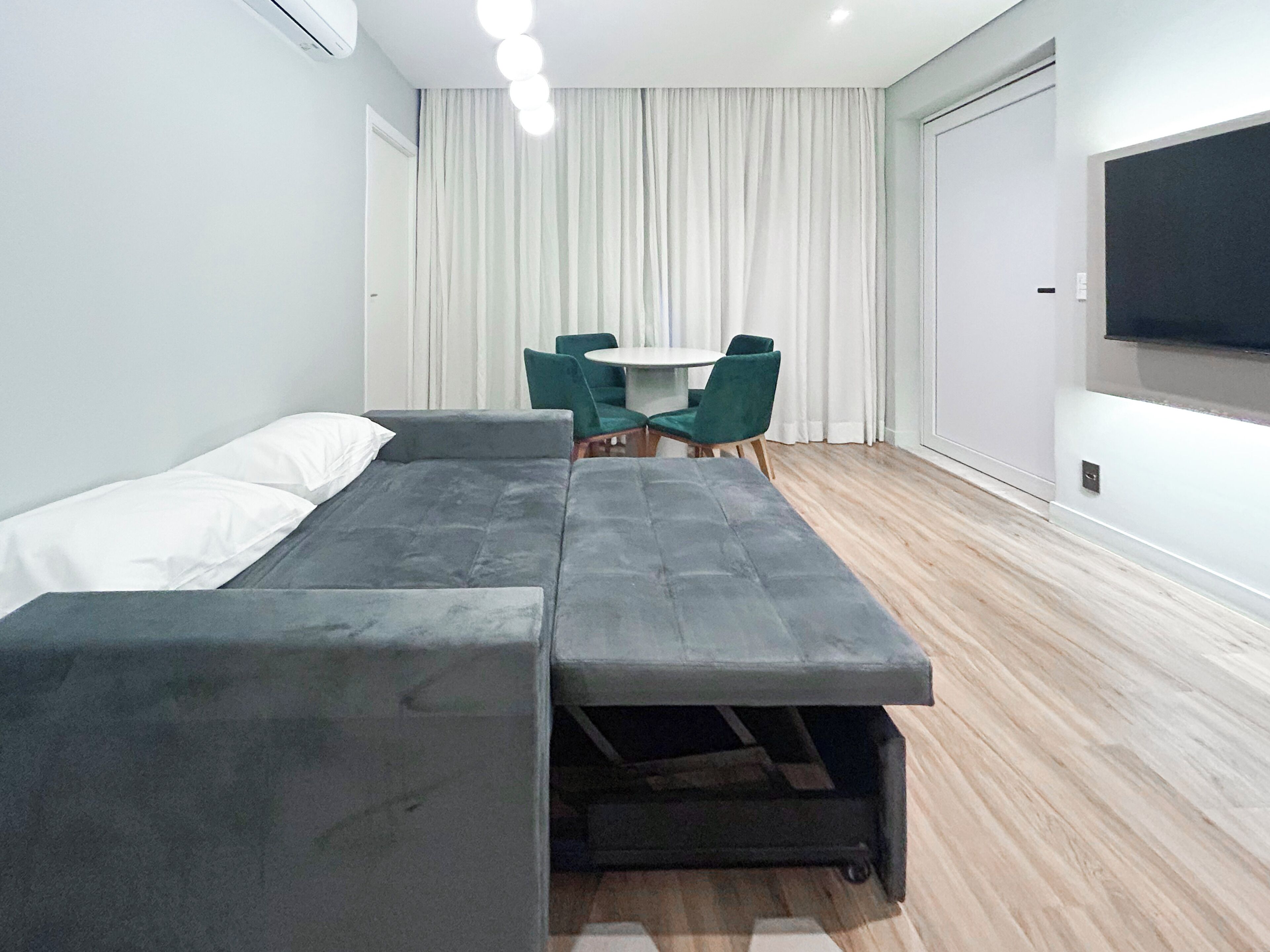 Quarto moderno com cama, uma mesinha, cadeiras e televisão.