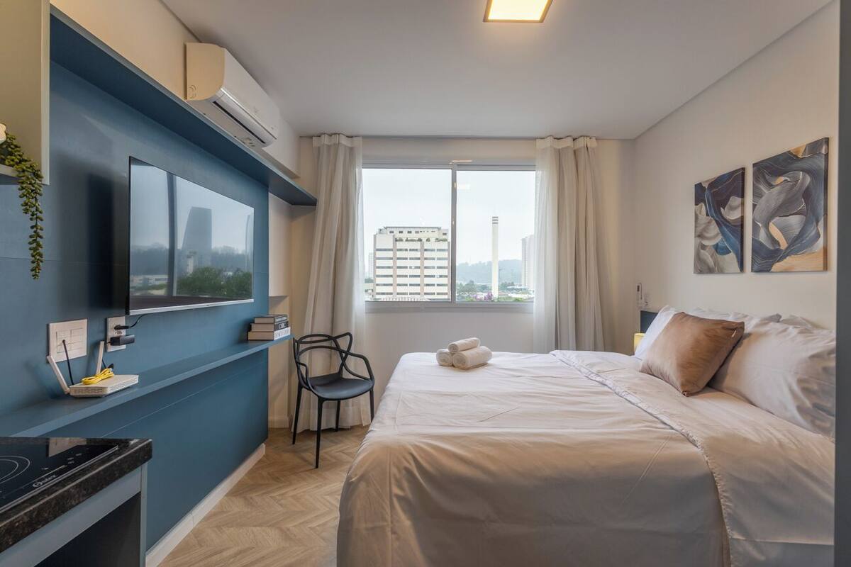 Une chambre d’hôtel moderne dotée d’un grand lit, d’un téléviseur à écran plat fixé au mur, d’un bureau avec un ordinateur et d’une fenêtre donnant sur la ville.