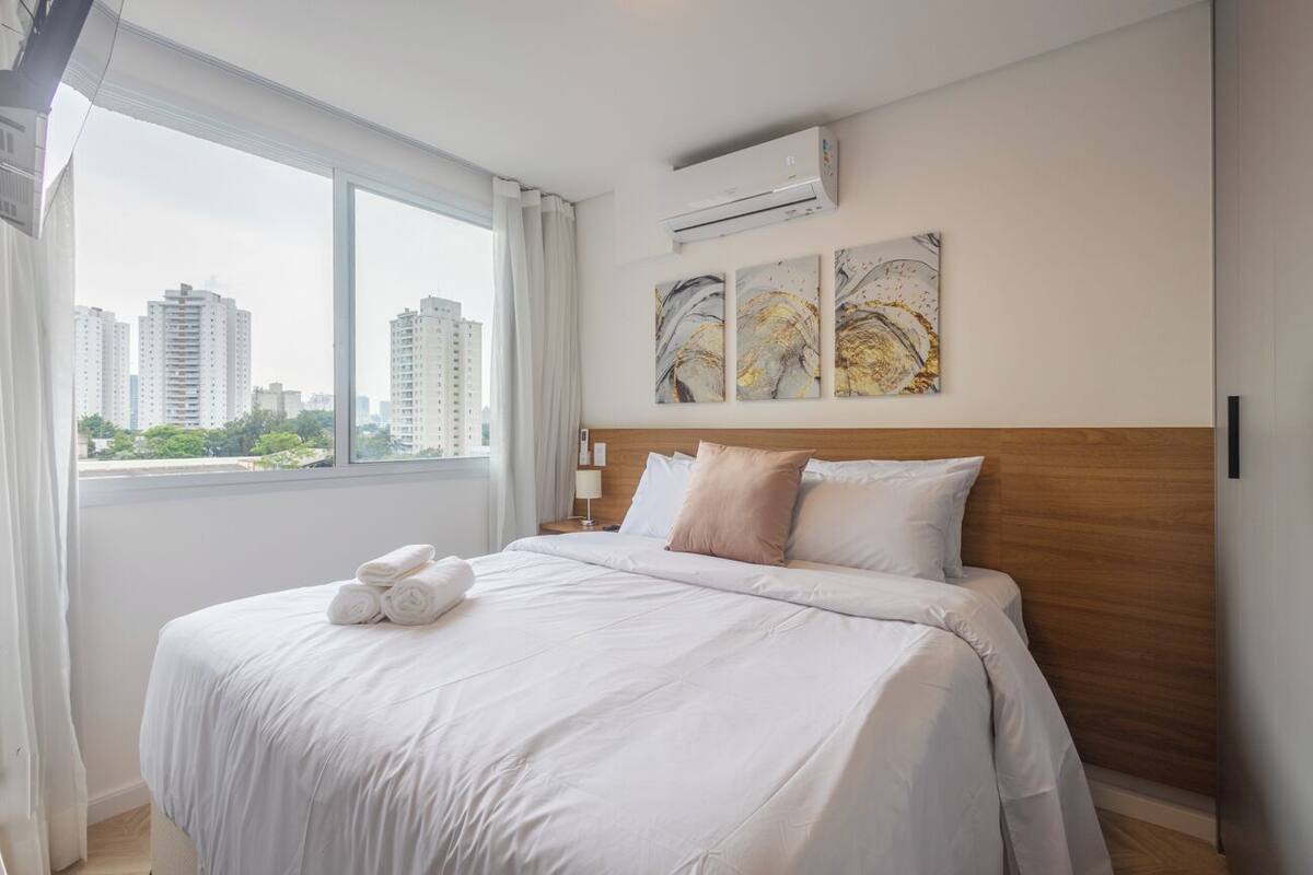 Une chambre d’hôtel avec un grand lit, une tête de lit en bois et une vue sur la ville par la fenêtre.