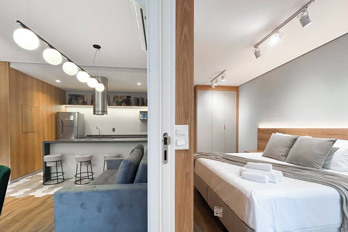 Une chambre d’hôtel moderne comprenant un lit, une kitchenette, un coin salon avec des tabourets et un mur décoratif en bois.