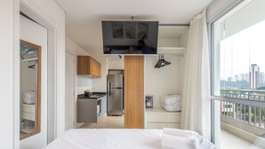 Une chambre d’hôtel moderne dotée d’un grand lit, d’un téléviseur fixé au mur, d’un coin cuisine et d’un balcon offrant une vue sur la ville.