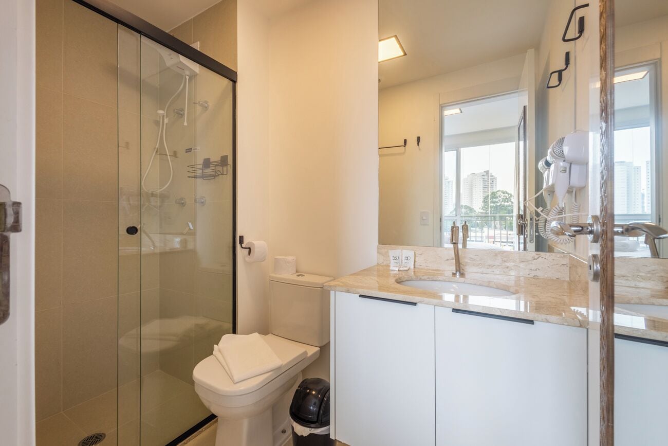 Een moderne badkamer met een douchecabine van glas, een toilet, een wastafel met spiegel en een haardroger op het aanrecht.