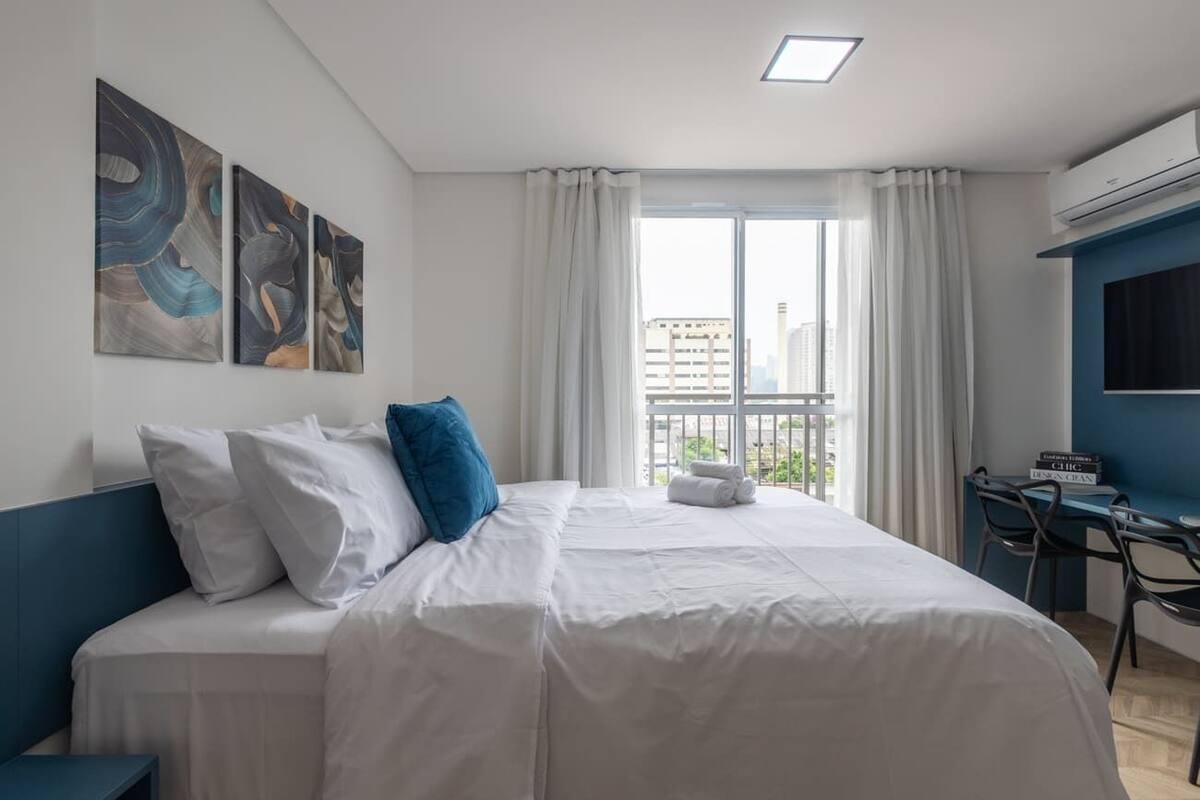 Une chambre d’hôtel avec un grand lit, du linge de lit blanc, un bureau avec des chaises et une vue sur la ville par une grande fenêtre.