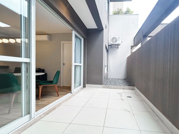 A modern interior with a sliding glass door leading to a dining area, a small seating space, and a grey exterior wall.