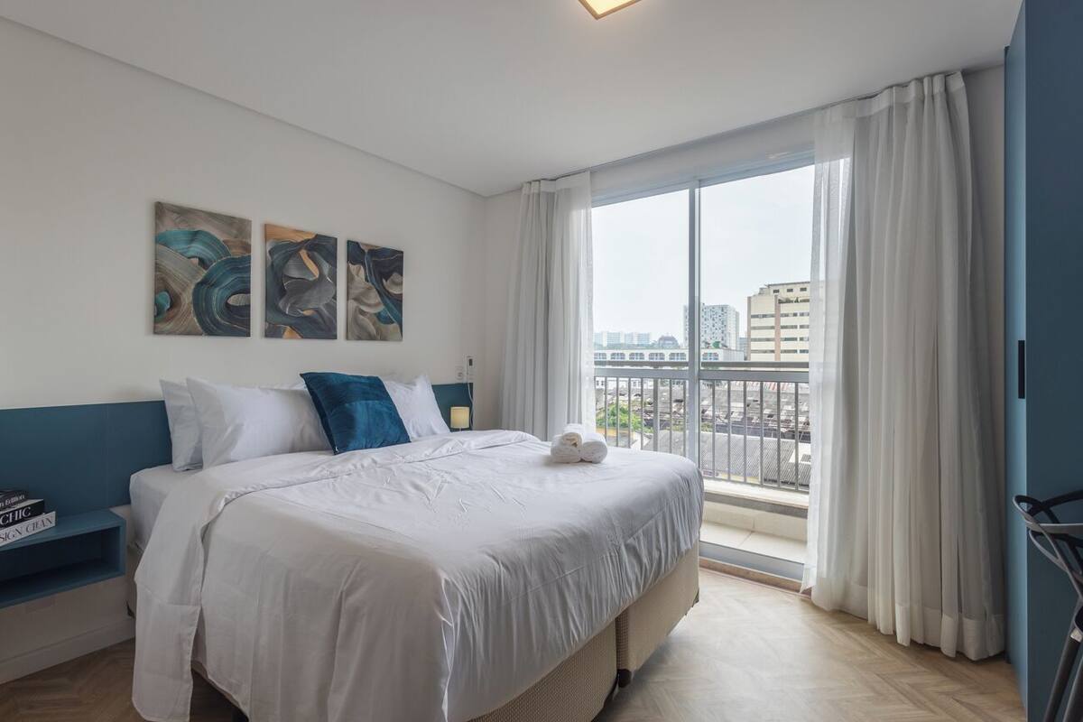 Une chambre d’hôtel avec un grand lit, une vue sur la ville par la fenêtre et des œuvres d’art accrochées au mur.