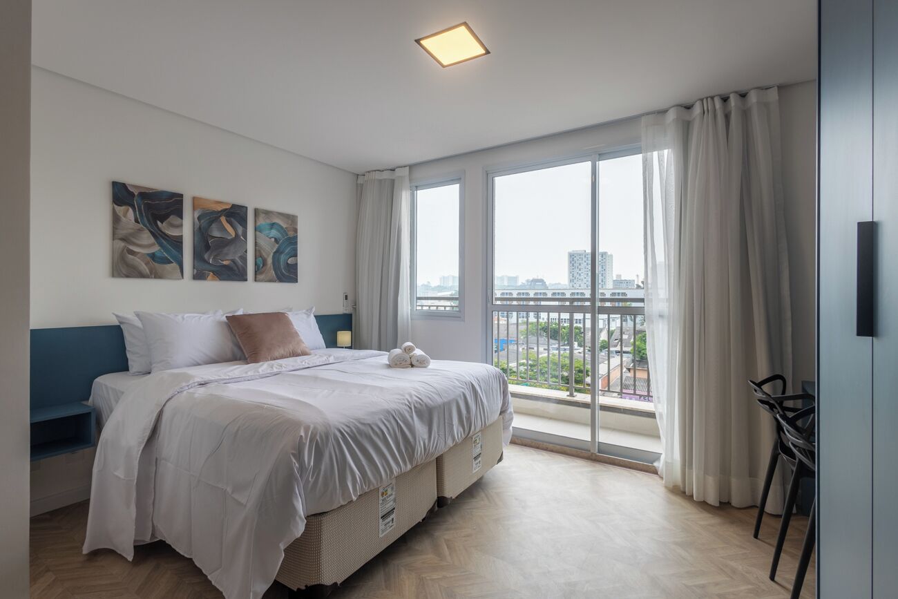 Quarto moderno com uma cama grande, vista para a cidade e uma varanda com uma cadeira.