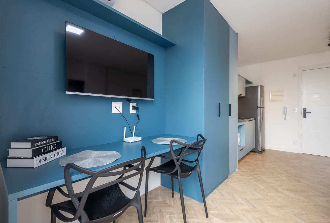 A modern kitchen with a blue accent wall, a flat-screen TV, and a dining area with two chairs and a table.