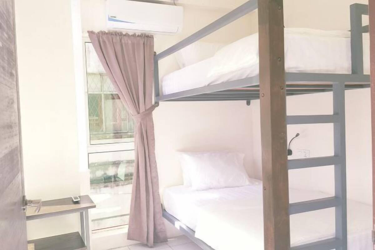 A bunk bed room with a window, curtains, and a small table.