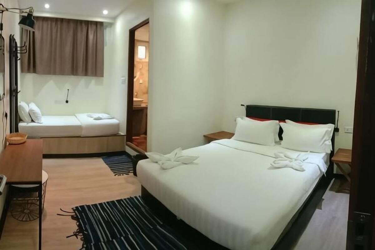 A hotel room with a bed, a desk, a chair, a lamp, and a window.