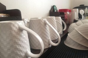A kitchen area with white mugs and plates on a shelf. - Kuree Hut (Semporna)